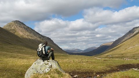 Hill walker sitting on a rock admiring the view of a u-shaped valley in Glen Coe