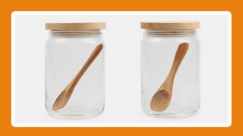 A glass jar filled with a white viscous material, and a wooden spoon on a table top.