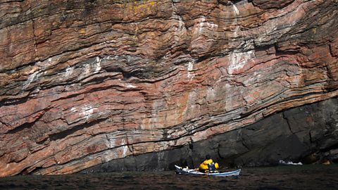 A person sea kayaking past cliffs of gneiss