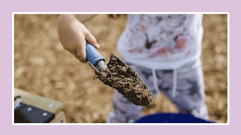 A child holding a garden trowel with soil.