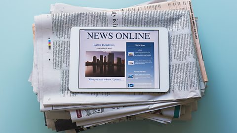 An image of a tablet computer on top of a stack of newspapers