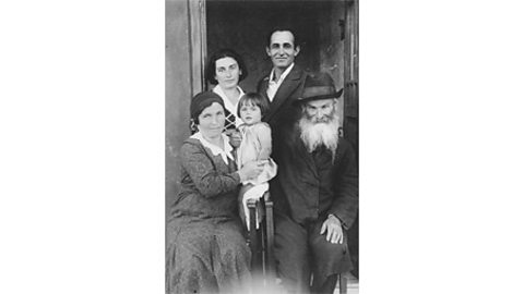 A black and white photograph of five Jewish family members sitting outside their house.