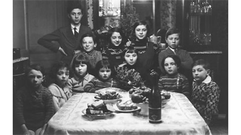 A black and white photograph of a group of Jewish children gathered around a table at a birthday party.