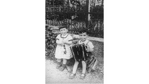 A black and white photograph of two small children playing musical instruments in their garden.