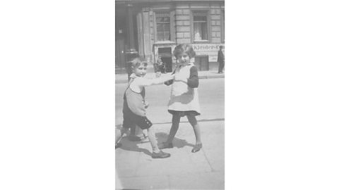 A black and white photograph of young twins playing outside in the street.