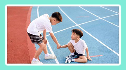 One young boy helping another boy off the floor