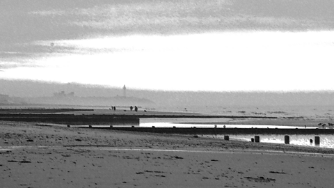 An image of a long beach with wooden posts leading out into the sea.