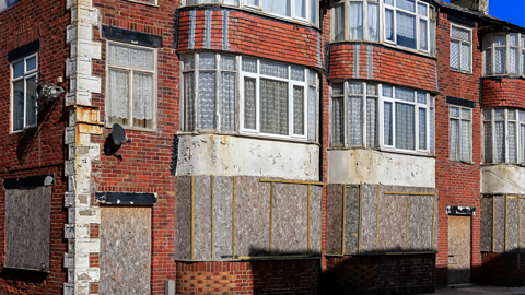 A building which is boarded up across the windows and doors and appears dilapidated.