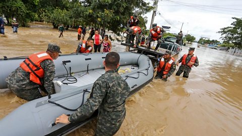 People in army clothing push an inflatable boat through flood waters
