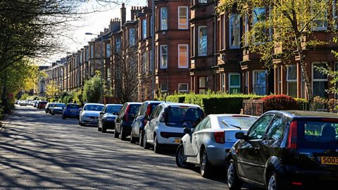 A minor road along a residential street in Govan. Cars are parked in a line along the road.