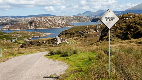 A passing place and single track road with views of a loch and mountains