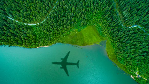 The shadow of a passenger plane on a lake next to a large forest.