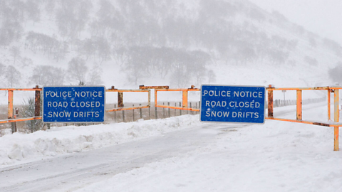 Snow gates on the A93 on a very snowy day. Signs read 'Police Notice Road Closed Snow Drifts'