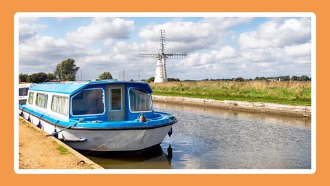 A canal boat on the Norfolk broads with fields and a windmill as a backdrop