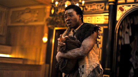 The Black British actor Fisayo Akinade stands onstage during a production of The Tempest, clutching some material to his chest.