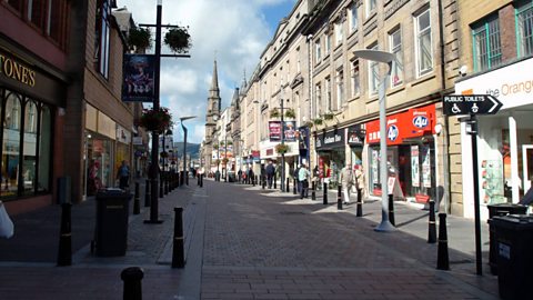 A high street with shops and cafes. People are walking along the street. 