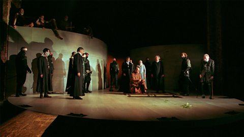 Friar Lawrence kneels on the floor surrounded by several characters wearing black. 