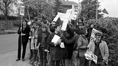 A black and white photograph of a group of university students holding protest signs