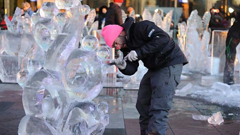 Photograph of a man in a pink hat carving an abstract ice sculpture