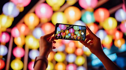 Hands holding a phone on camera setting. Chinese lanterns visible in the phone's screen