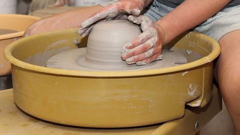 A pair of hands working a solid piece of clay on a potter's wheel