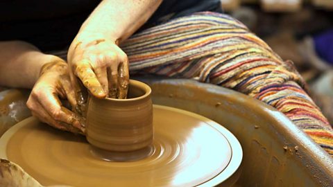 A pair of hands working on forming a pot on a potter's wheel