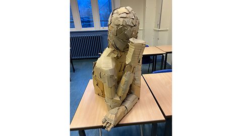 Cardboard sculpture of a human torso and head on a school desk