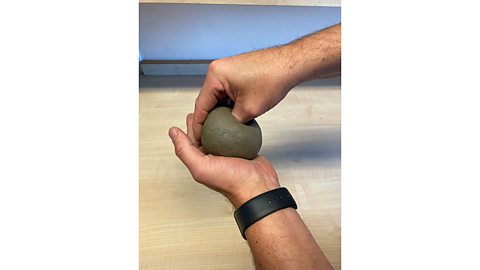 A ball of clay in the palm of a left hand with the thumb of the right hand stuck into it