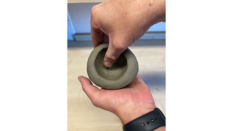 A piece of clay in a pair of hands in the process of being formed into a bowl