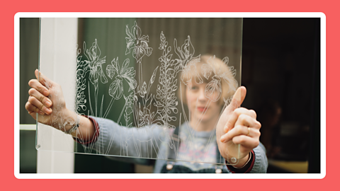 A person holding up a piece of glass that has a flowery design etched onto it.