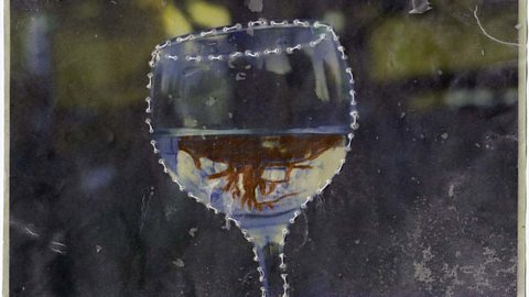 A photograph of a wine glass. The liquid in the glass has been painted over and the outlines of the glass have been sewn along