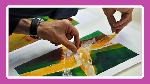 A close up shot of hands placing coloured plastic and paper onto a canvas.