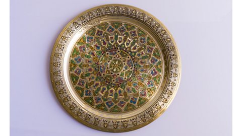 A decorative metal plate with a colourful geometric pattern, against a white background