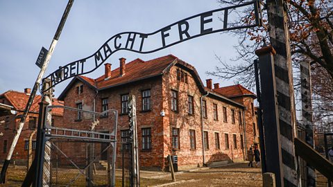 A photograph of the entrance to Auschwitz, showing the sign that reads 'Arbeit macht frei' (work sets you free) in German.