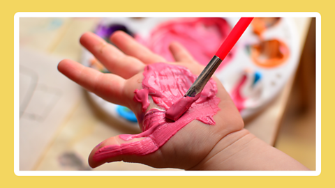 A palm of a hand being covered with pink paint. 