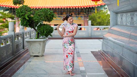 A barefoot woman holding a fan and wearing a pink floral dress of Chinese design