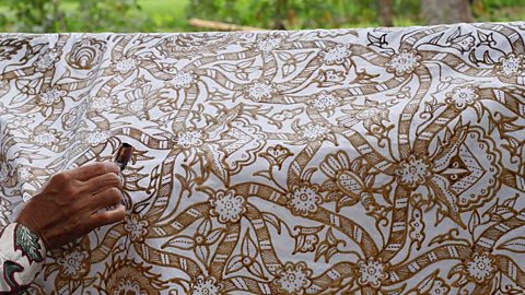 A hand painting brown floral patterns onto white cloth