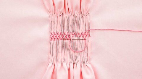 A design being sewn into pink fabric by smocking