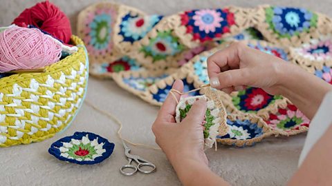 Multi-coloured yarns in a basket. A woman crocheting a baby blanket.