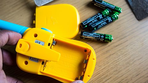 A toy walk talkie with its AAA batteries removed, visible on the table.