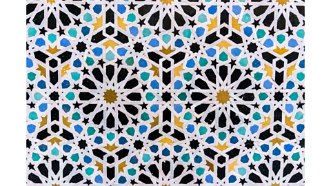 Intricate tile patterns on a floor in yellow, green and blue, showing tiled patterns like stars and hexagons.