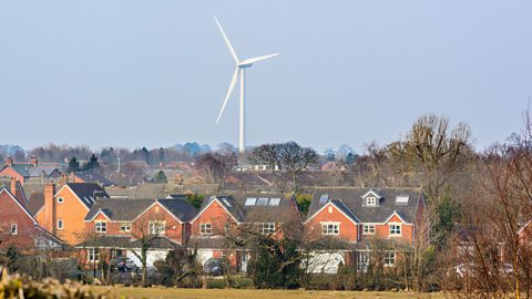 A wind turbine in the background and houses in front of it.