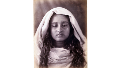 A black and white photograph showing a girl facing the camera, looking below it, with cloth surrounding her head and shoulders.