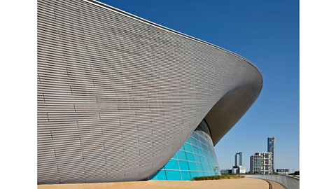 A grey curvy building, one side built with window panes.