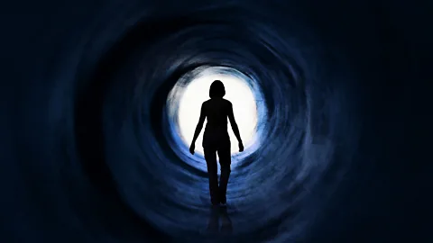 A person walking down a tunnel towards a bright light.