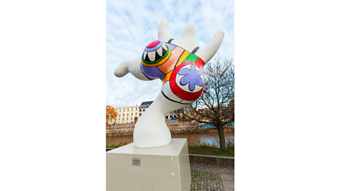 A Nana by Niki de Saint Phalle, stood on top of a block and consisting of bright colours.