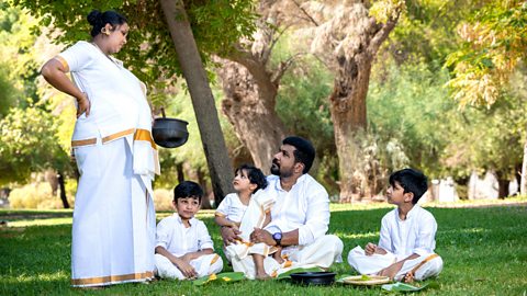 Christian Kerala family  - the pregnant wife serves food to her husband and children as they sit on the grass in a park.