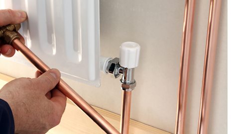 A plumber installing a new radiator using copper pipes