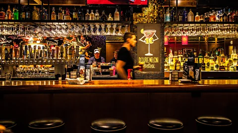 A bartender walking behind a bar, holding a beer