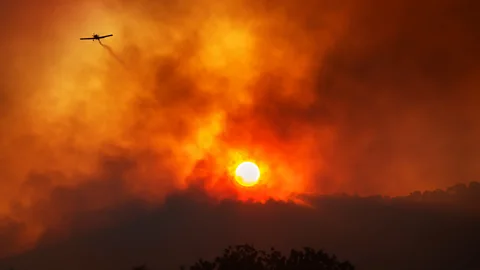 A plane flying over a wildfire with the sun shrouded in smoke (Credit: Getty Images)